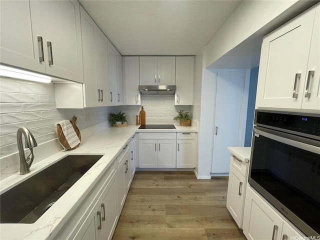1561 Kanunu St Unit 1206, Honolulu, HI 96814 - kitchen with stainless steel oven, a sink, under cabinet range hood, white cabinets, and black electric stovetop