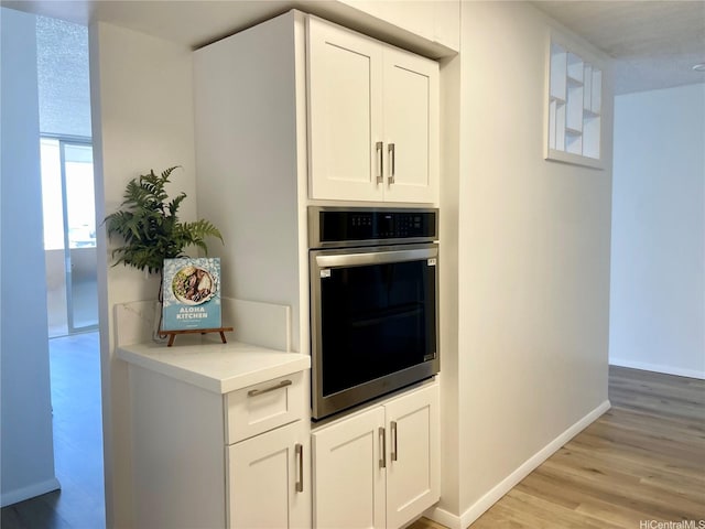 1561 Kanunu St Unit 1206, Honolulu, HI 96814 - kitchen featuring stainless steel oven, light wood-type flooring, baseboards, light countertops, and white cabinetry