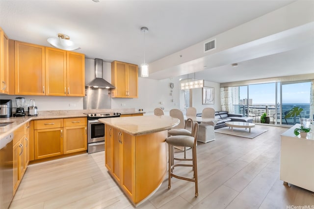 kitchen with wall chimney exhaust hood, stainless steel appliances, light wood-type flooring, open floor plan, and a center island