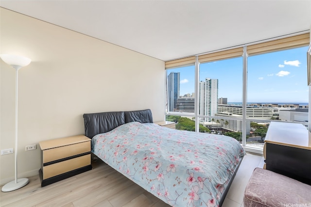 bedroom with a view of city, wood finished floors, floor to ceiling windows, and baseboards