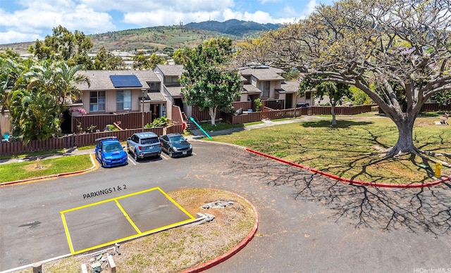 92-1044 Kanehoa Loop Unit 84, Kapolei, HI 96707 - view of front of property featuring uncovered parking, a mountain view, solar panels, fence, and a shingled roof