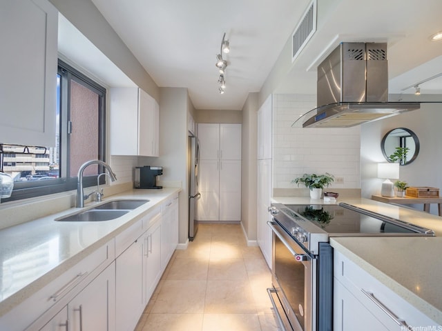kitchen with stainless steel appliances, island range hood, a sink, track lighting, and white cabinets