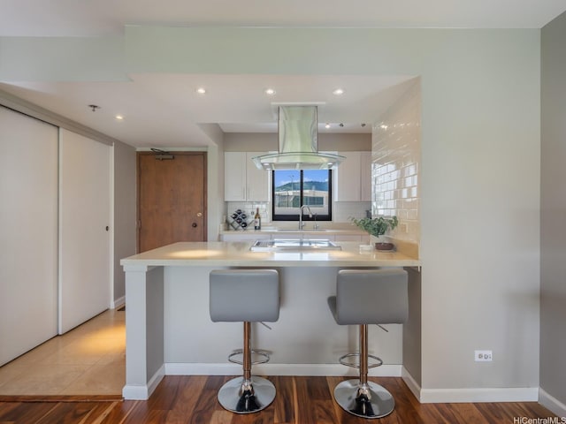 kitchen featuring light countertops, white cabinets, a sink, a kitchen bar, and recessed lighting