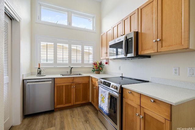 kitchen with stainless steel appliances, a sink, light wood-style flooring, and light countertops