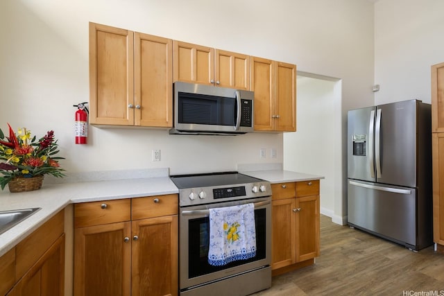 kitchen featuring appliances with stainless steel finishes, light wood-style floors, light countertops, and brown cabinets