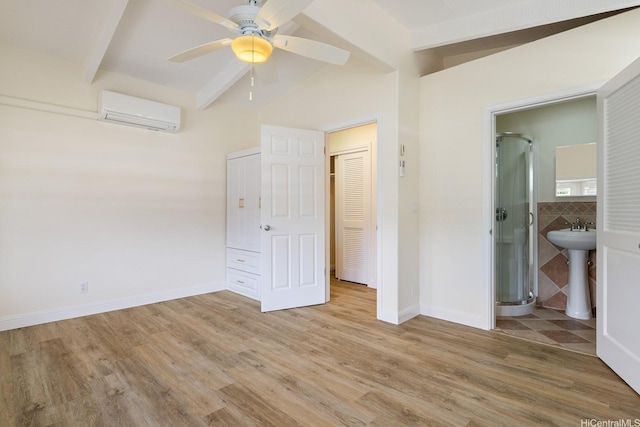 unfurnished bedroom with a wall mounted AC, light wood-type flooring, baseboards, ensuite bath, and a ceiling fan