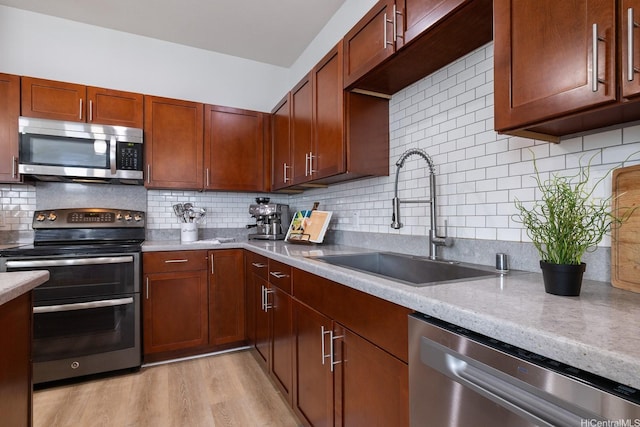 kitchen featuring appliances with stainless steel finishes, a sink, decorative backsplash, and light wood-style floors