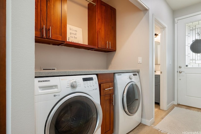 washroom featuring washer and dryer, light wood-style flooring, cabinet space, and baseboards