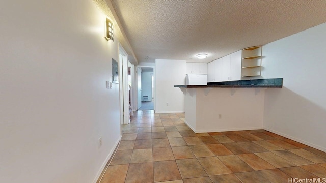 kitchen featuring open shelves, refrigerator, dark countertops, a peninsula, and a kitchen breakfast bar