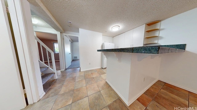 kitchen with open shelves, freestanding refrigerator, white cabinets, a breakfast bar area, and a peninsula