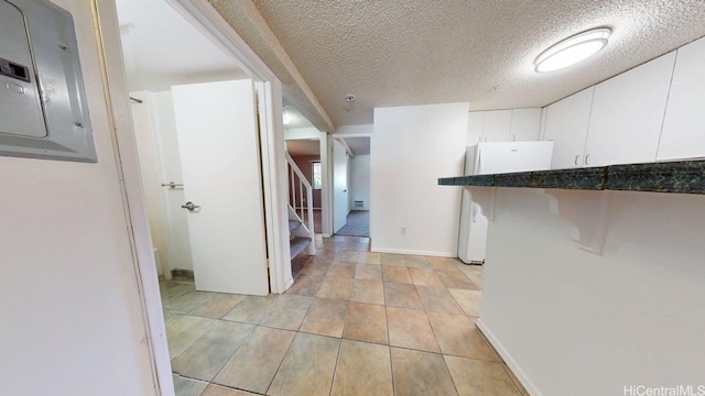 kitchen with electric panel, white cabinetry, freestanding refrigerator, and a textured ceiling