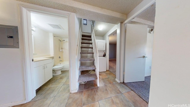 bathroom featuring stacked washer / drying machine, electric panel, toilet,  shower combination, and tile patterned flooring