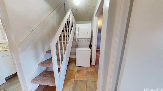 stairway with stacked washing machine and dryer and a textured ceiling