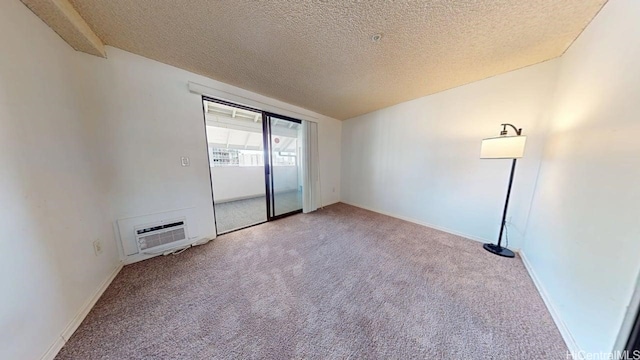 spare room with light colored carpet, a wall unit AC, a textured ceiling, and baseboards