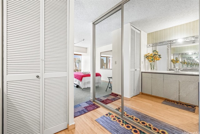 hall with wood finished floors, a textured ceiling, a sink, and baseboards