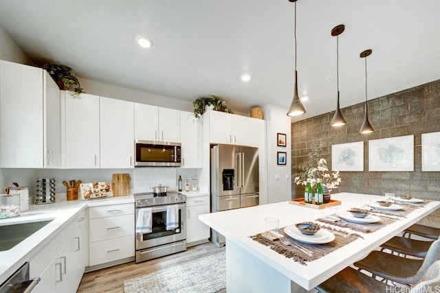 kitchen with appliances with stainless steel finishes, a breakfast bar area, backsplash, light countertops, and white cabinets