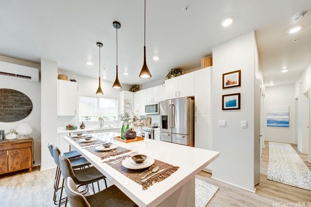 kitchen with stainless steel appliances, a wall mounted air conditioner, light wood-type flooring, light countertops, and a kitchen breakfast bar