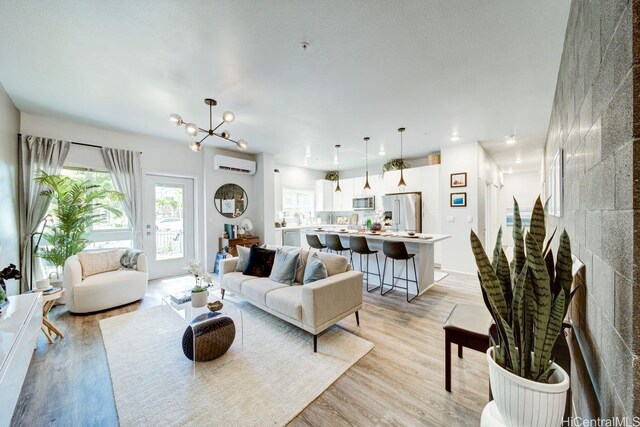 living room with a wall mounted air conditioner, light wood-style flooring, and a chandelier