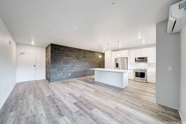 kitchen with appliances with stainless steel finishes, open floor plan, an AC wall unit, white cabinets, and light wood-style flooring