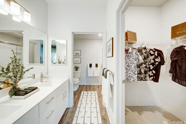 bathroom featuring toilet, a shower with door, double vanity, and wood finished floors
