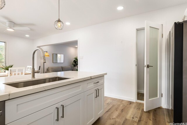 98-508 Kamahao Pl Unit 68, Pearl City, HI 96782 - kitchen featuring a sink, light wood-type flooring, white cabinets, light stone countertops, and pendant lighting