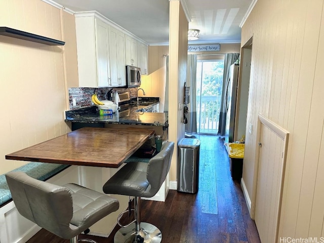 1023 Kapahulu Ave Unit 1, Honolulu, HI 96816 - kitchen with stainless steel microwave, dark wood finished floors, backsplash, white cabinets, and ornamental molding
