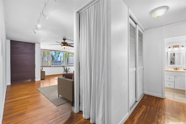 hallway with wood finished floors, baseboards, and rail lighting