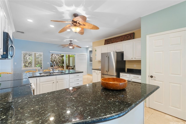 kitchen with a sink, high end fridge, ceiling fan, white cabinets, and dark stone counters