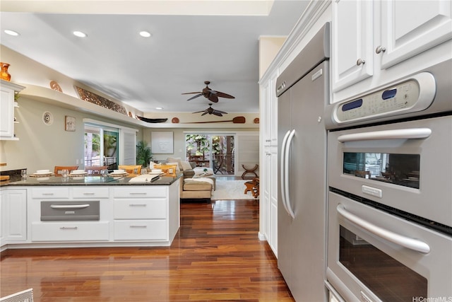 kitchen featuring stainless steel built in refrigerator, a peninsula, dark countertops, wood finished floors, and a ceiling fan