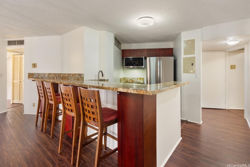 1088 Bishop St Unit 3007, Honolulu, HI 96813 - kitchen with appliances with stainless steel finishes, dark wood finished floors, a breakfast bar, a peninsula, and a textured ceiling
