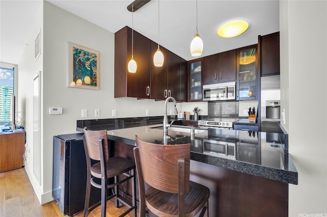 1189 Waimanu St Unit 1606, Honolulu, HI 96814 - kitchen featuring appliances with stainless steel finishes, dark brown cabinetry, glass insert cabinets, and a peninsula