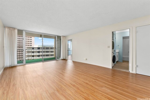 3020 Ala Napuaa Pl Unit 103, Honolulu, HI 96818 - spare room with stacked washer / drying machine, wood finished floors, a textured ceiling, a wall of windows, and baseboards