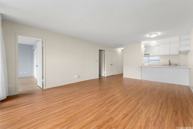 3020 Ala Napuaa Pl Unit 103, Honolulu, HI 96818 - unfurnished living room with light wood finished floors, a sink, a textured ceiling, and baseboards