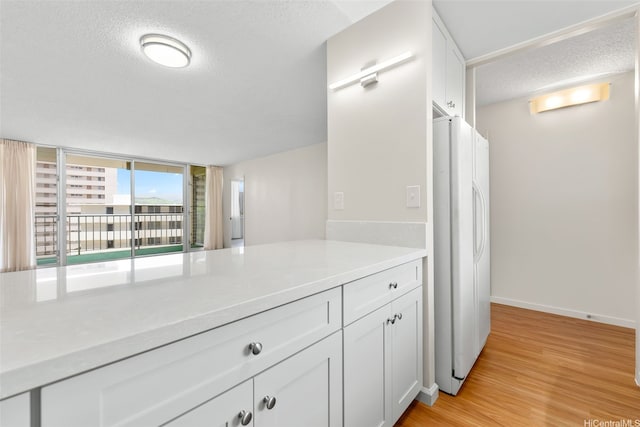 3020 Ala Napuaa Pl Unit 103, Honolulu, HI 96818 - kitchen with freestanding refrigerator, a textured ceiling, light countertops, white cabinetry, and light wood-type flooring