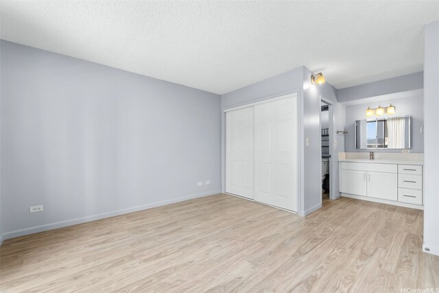 3020 Ala Napuaa Pl Unit 103, Honolulu, HI 96818 - unfurnished bedroom featuring light wood-type flooring, a textured ceiling, a closet, a sink, and baseboards