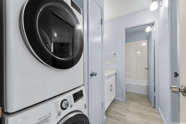 3020 Ala Napuaa Pl Unit 103, Honolulu, HI 96818 - laundry area featuring estacked washer and dryer, light wood-style flooring, a textured ceiling, and baseboards