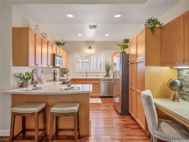 95-1073 Loea St, Honolulu, HI 96789 - kitchen featuring appliances with stainless steel finishes, a peninsula, a sink, light wood-style floors, and a kitchen breakfast bar