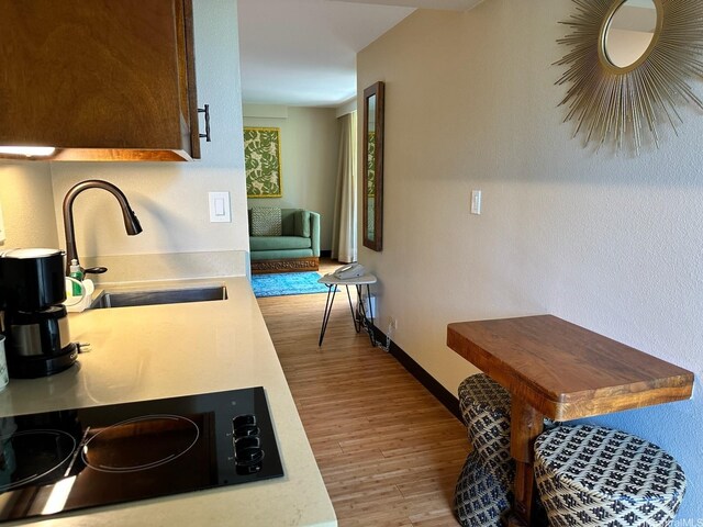 2425 Kuhio Ave Unit 410, Honolulu, HI 96815 - kitchen with black electric stovetop, wood finished floors, a sink, light countertops, and baseboards