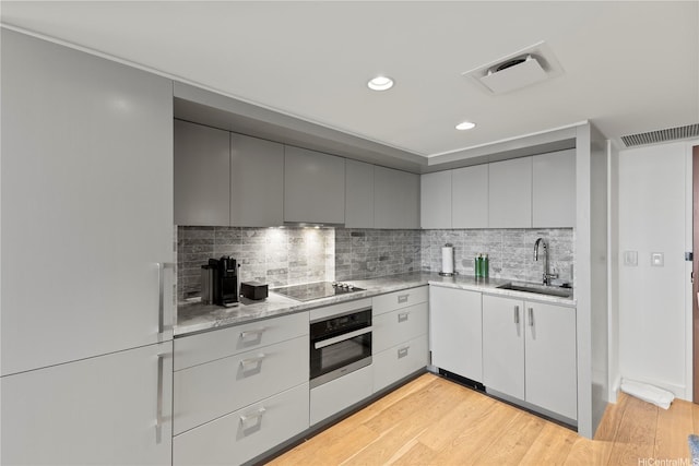 383 Kalaimoku St Unit E1111, Honolulu, HI 96815 - kitchen featuring stainless steel oven, a sink, black electric cooktop, tasteful backsplash, and light wood-type flooring