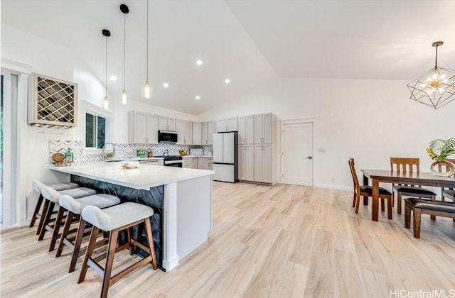 kitchen with stainless steel appliances, a peninsula, light countertops, a kitchen breakfast bar, and vaulted ceiling