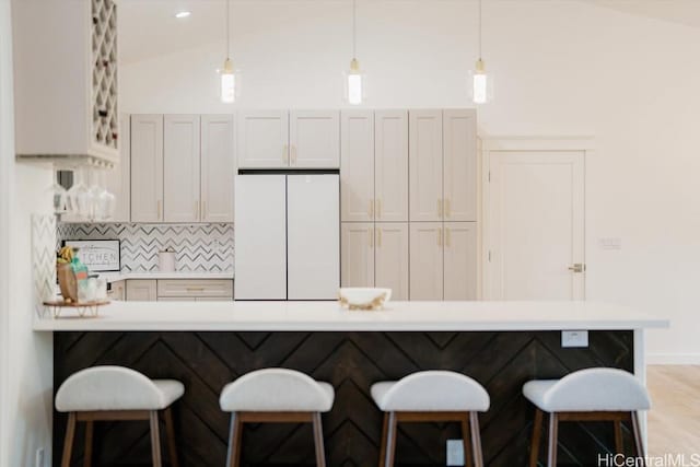 kitchen with freestanding refrigerator, decorative backsplash, light countertops, a kitchen breakfast bar, and pendant lighting