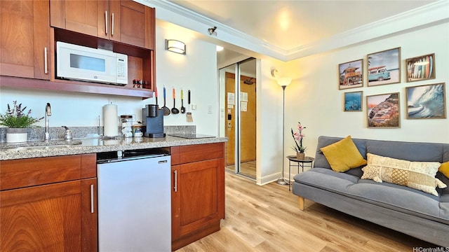 2425 Kuhio Ave Unit 603, Honolulu, HI 96815 - kitchen featuring white microwave, a sink, light wood-type flooring, crown molding, and light stone counters
