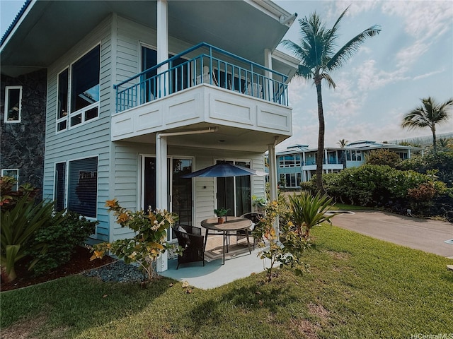 rear view of property with a balcony, a lawn, and a patio area