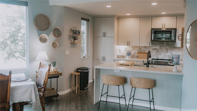kitchen featuring dark wood-style floors, light countertops, a kitchen breakfast bar, tasteful backsplash, and baseboards