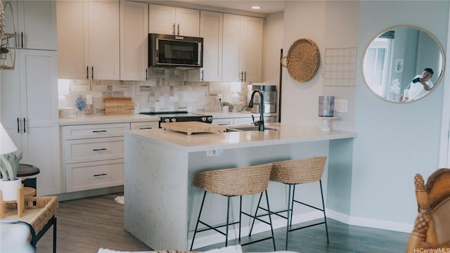 kitchen with black microwave, a sink, stove, tasteful backsplash, and dark wood-type flooring