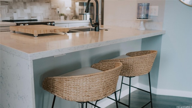 kitchen with a sink, a breakfast bar area, light stone counters, decorative backsplash, and white cabinetry