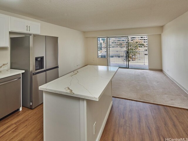 1333 Heulu St Unit 408, Honolulu, HI 96822 - kitchen featuring appliances with stainless steel finishes, wood finished floors, a kitchen island, light stone countertops, and a textured ceiling