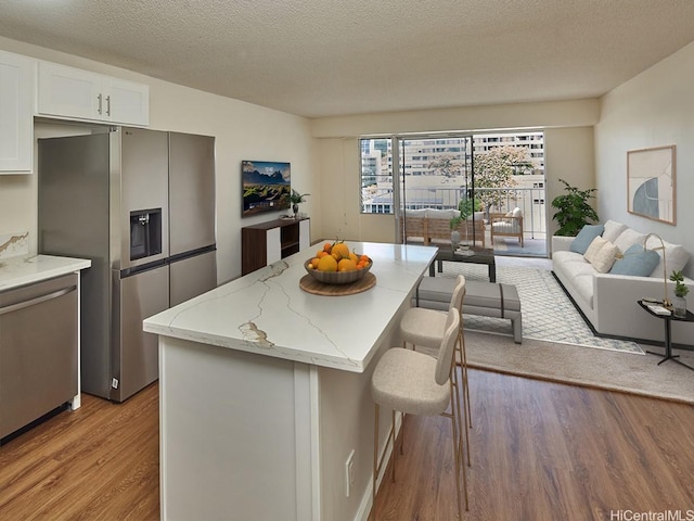 1333 Heulu St Unit 408, Honolulu, HI 96822 - kitchen featuring appliances with stainless steel finishes, wood finished floors, a kitchen bar, light stone counters, and a center island