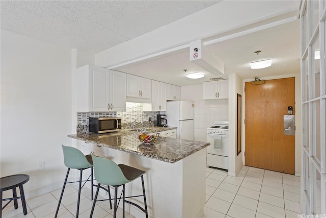 1777 Ala Moana Blvd Unit 1517, Honolulu, HI 96815 - kitchen with white appliances, dark stone countertops, a peninsula, tasteful backsplash, and light tile patterned flooring