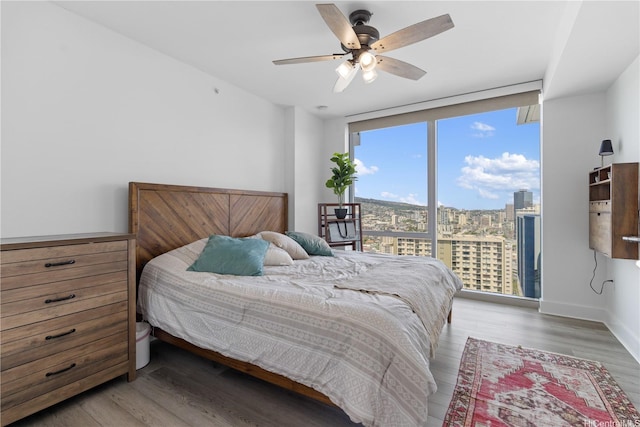 629 Keeaumoku St Unit 2505, Honolulu, HI 96814 - bedroom featuring floor to ceiling windows, wood finished floors, a view of city, a ceiling fan, and baseboards